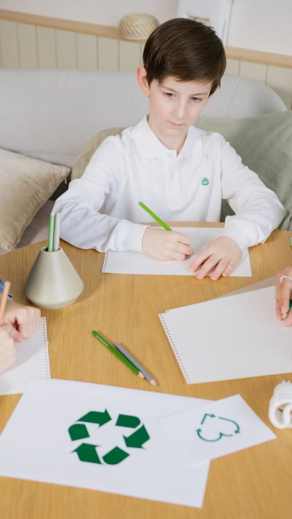 A young boy drawing recycling symbols on paper, promoting sustainability indoors.